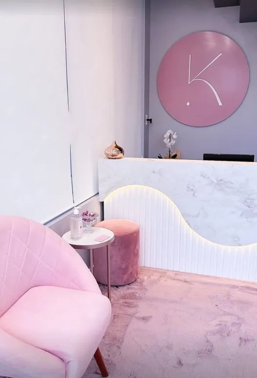 Recepção com poltrona rosé, balcão de mármore e o monograma K na parede